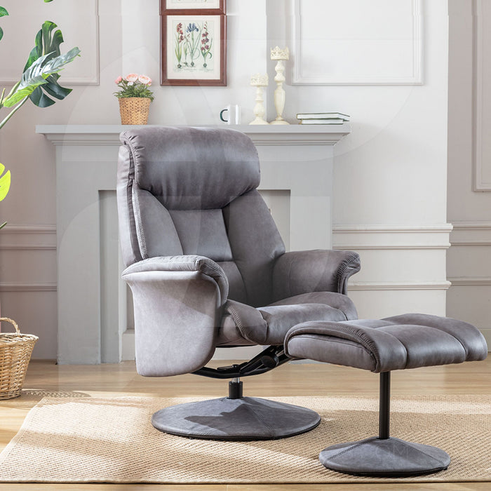 A modern gray Kenmare push back recliner with a matching footstool rests on a woven rug in a cozy living room with a white mantel decorated with accents and a nearby potted plant.