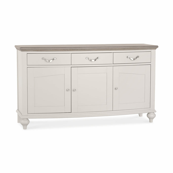 The Montreux Large Sideboard features a white wooden frame, three top drawers, three lower cabinet doors with silver handles, a grey washed oak tabletop, short legs, and a classic elegant design.