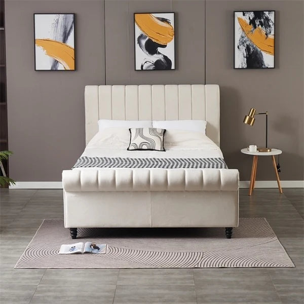 A modern bedroom featuring the Ascot Storage Bedframe in beige velvet, geometric bedding, a gray accent wall, three abstract art pieces above the bed, a gold lamp on a round side table, and a rug with an open magazine on the floor.