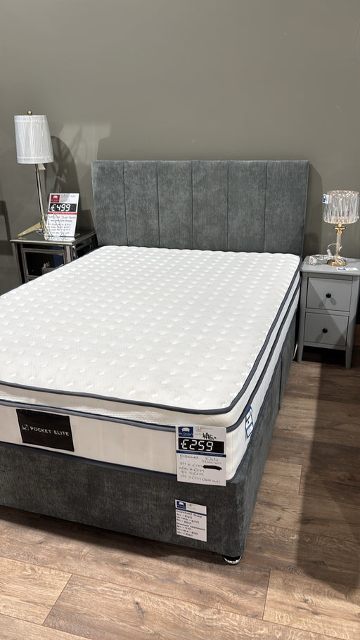 A Pocket Elite 1200 bed with a grey upholstered headboard and base, firm box top mattress, is showcased in a showroom between two nightstands with lamps. Price tags are displayed on the bed and nightstands.