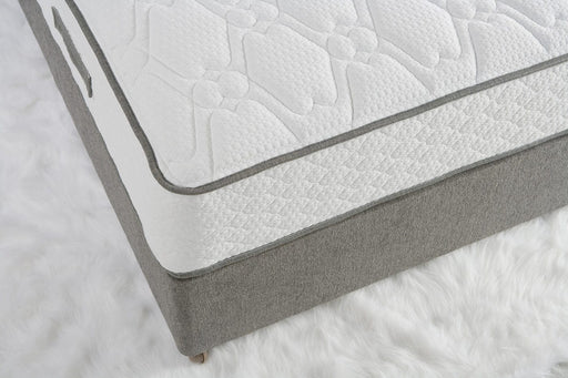 A close-up of the King Koil Paradise Mattress shows its white textured top, gray sides, and Flex-edge border supports, placed on a fluffy white rug.