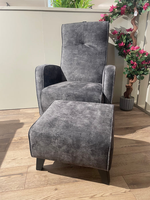 The gray Kelvin Chair and its matching footstool rest on a wooden floor, with pink flowers and greenery in the background as sunlight streams down.