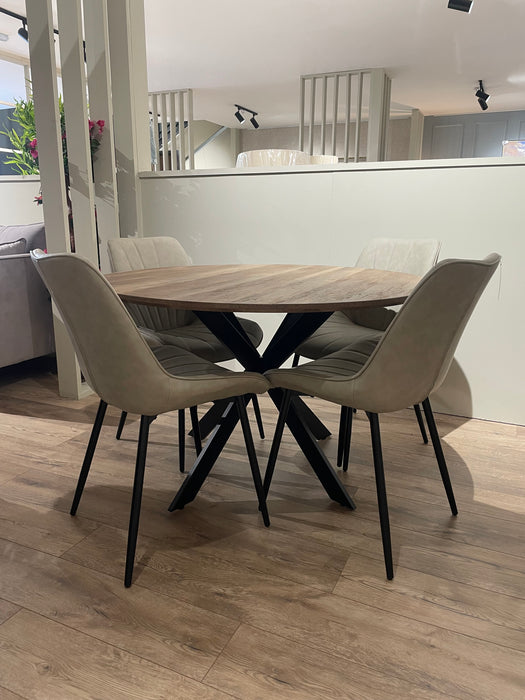 The Elson Round Dining Table with black X legs is paired with four light beige cushioned chairs on a wooden floor in a bright, modern room.