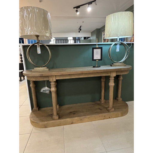 Long, rustic-style hallway table displayed in a furniture showroom, topped with two identical lamps with circular metal bases and natural fabric shades.