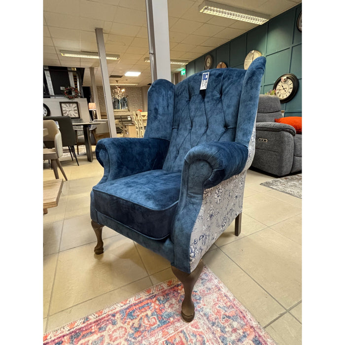 The Buttoned Back Queen Anne Chair features blue velvet upholstery, a tufted backrest, and floral-patterned side panels. Available in a furniture showroom with Irish-made pieces, a full fabric range, plus chairs, tables, and clocks.