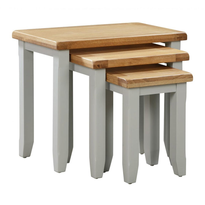 The Capri nest of tables by vendor-unknown features three wooden tables with oak tops and light grey legs, designed to neatly nest in descending size order for space-saving storage.