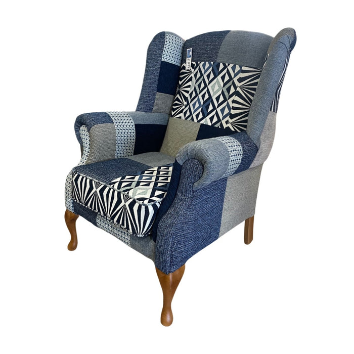 The Queen Anne Chair features winged sides and sturdy wooden legs, upholstered in blue, gray, and black geometric patchwork. Irish made for style and comfort, it is inspired by classic design.