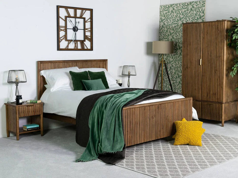 A modern bedroom with a Cairo Wide Chest, wooden bed, white bedding, green and white pillows, green throw, bedside tables with lamps, wardrobe, floor lamp, wall clock, and a yellow star cushion on a gray rug.