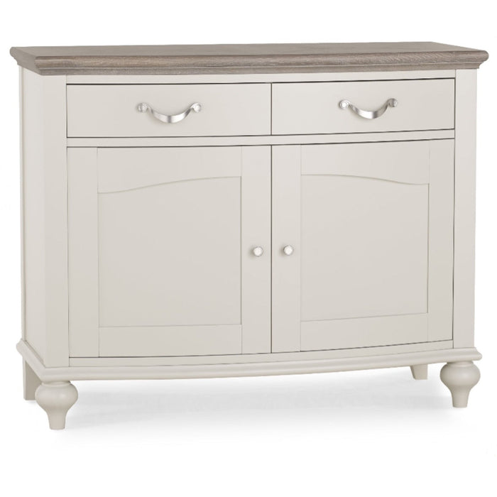 The Montreux Small Sideboard features a light gray washed oak finish, dark wood top, two drawers with metal handles, two lower cabinet doors with round knobs, and stands on four short legs.