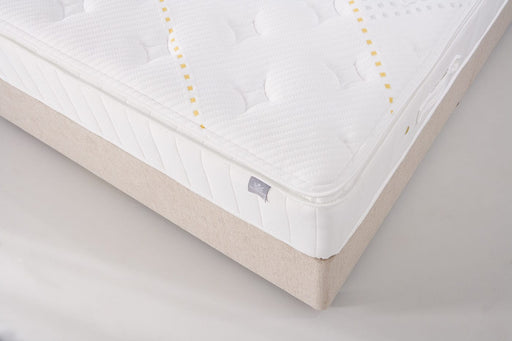 Close-up of the King Koil - Spinal Pocket Pillow Top, a white quilted mattress with subtle pattern and stitched detailing on a light beige bed base. Features a small side label and offers excellent support.