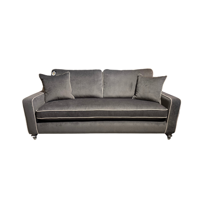 The Emperor Range sofa is a modern dark gray velvet suite with white piping, angled armrests, two matching throw pillows, and crafted from Aqua Clean fabrics, shown against a white background.