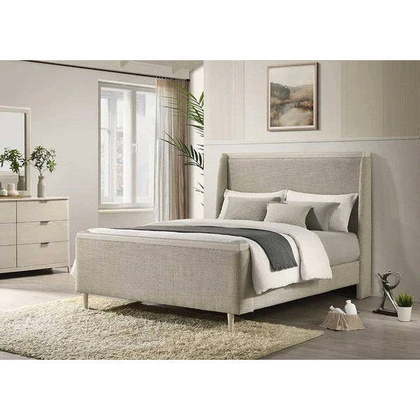 A modern bedroom with a taupe fabric headboard and neutral bedding on the Parma Bedframe in light ash. There’s a dresser with a mirror and plant, a soft rug, premium bedroom furniture, wall art, and sunlight through sheer curtains.