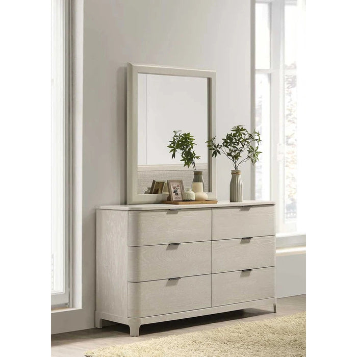 The Parma Wide Chest, crafted from light ash wood with six soft-closing drawers, stands against a white wall. A large mirror rests atop it, surrounded by plants, framed photos, and decor as sunlight streams through nearby windows.