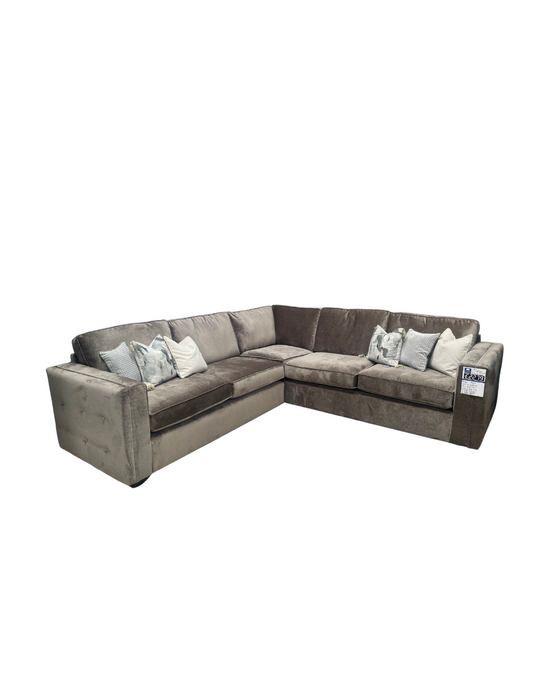 The Ariya sofa is a spacious L-shaped sectional in gray, designed for living room comfort with plush cushions and decorative throw pillows, shown isolated on a white background.