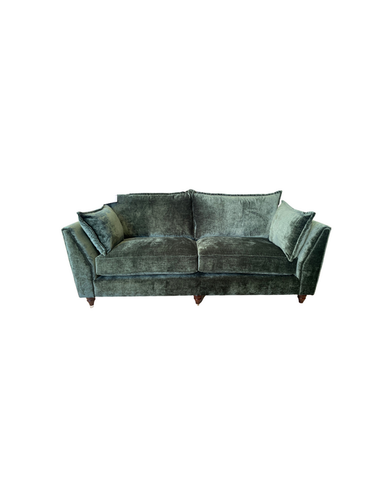 The Cleo Range dark green velvet sofa features deep seats, two seat and back cushions, and angular armrests. Its elegant style stands out beautifully against a white background.