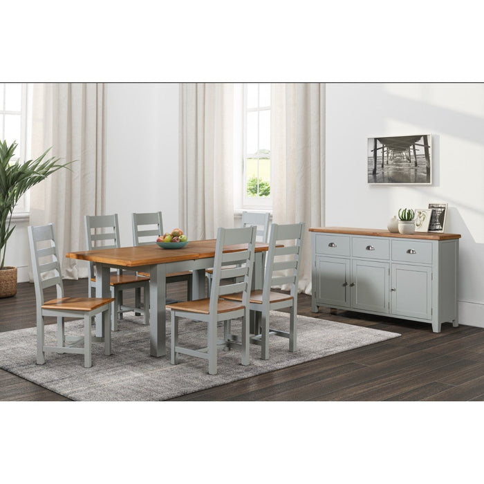 A modern dining room with a Capri Dining Table 140cm ext 180cm, six chairs with oak seats and Capri light grey frames, a grey sideboard with chrome cup handles and oak top, light curtains on two windows, and a grey rug under the table.