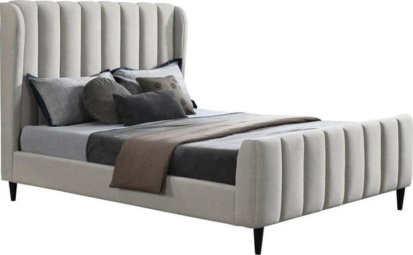 The Isobella Bedframe is a modern upholstered bed featuring a high headboard with vertical channel tufting in soft stone linen, styled with grey and black bedding, multiple pillows, and a folded brown blanket at the foot.