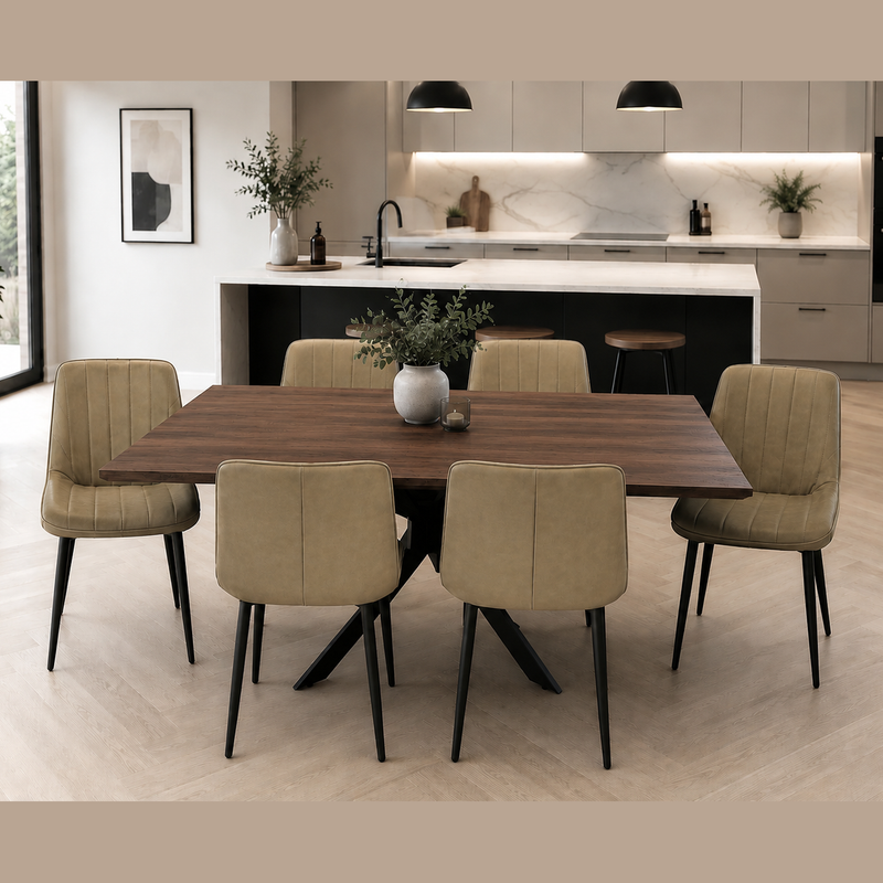 A modern dining area with the Elson Dark Table + 6 Lilly Chairs, black X legs, beige upholstery, and a potted plant centerpiece. A minimalist kitchen with pendant lights, marble backsplash, and light cabinetry is in the background.