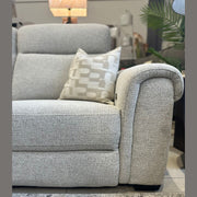 A close-up of the Luna Electric Recliner in light gray upholstery with a patterned cushion, set on a textured rug. A lamp and green plants in the background complete the cozy living room vibe.