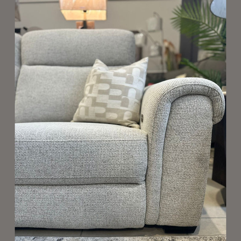 A close-up of the Luna Electric Recliner in light gray upholstery with a patterned cushion, set on a textured rug. A lamp and green plants in the background complete the cozy living room vibe.