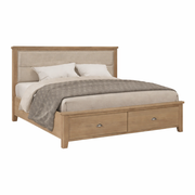 The Aylesbury bedframe offers a strong oak frame, an upholstered headboard, two pillows, a beige blanket, a gray throw, and two storage drawers at the foot.