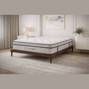 A neatly made bed with a gray and white Clifden Mattress rests on a wooden frame in a modern bedroom featuring white walls, a dresser, artwork, and tasteful decor.