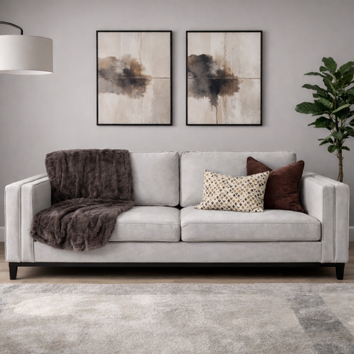 A modern living room with a Savannah 3+2 stone fabric sofa, throw pillows, a brown blanket, two abstract wall paintings, a floor lamp, potted plant, and a patterned rug on wooden floors.