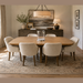 A dining room with an ash wood Ashton 2.1 Table and six beige Como chairs, centered by a glass vase, on a patterned rug, with a sideboard, wall art, and soft light from a lamp and chandelier.