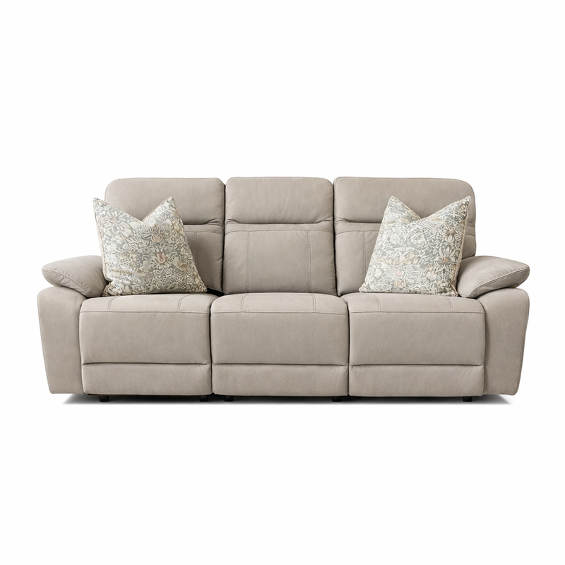 The Jude Recliner Sofa is a beige, three-seat sofa with plush armrests, a cushioned backrest, and two patterned throw pillows. Made from washable microfiber, it’s shown front-facing against a white background.