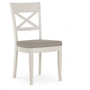 The Montreux Wooden Dining Chair features a white frame, X-shaped backrest, and a light gray cushioned seat, making it perfect for contemporary dining spaces. Shown against a plain white background.