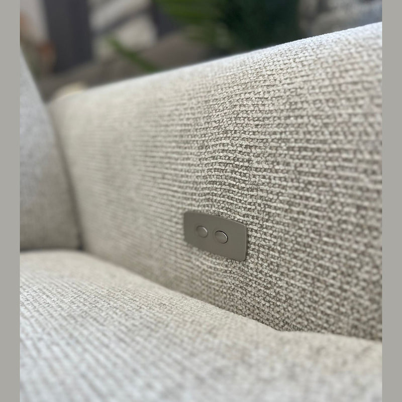 A close-up of the Luna Electric Recliner’s textured light gray fabric reveals a small metal panel with two round buttons, elegantly integrated into the side to showcase its powered reclining feature.