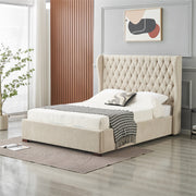 A modern bedroom showcases the Vienna Bedframe in beige fabric with a winged headboard, topped with white bedding and a black-and-white throw. A decorative pillow, artwork, indoor plant, and large window enhance the space’s bright neutral decor.
