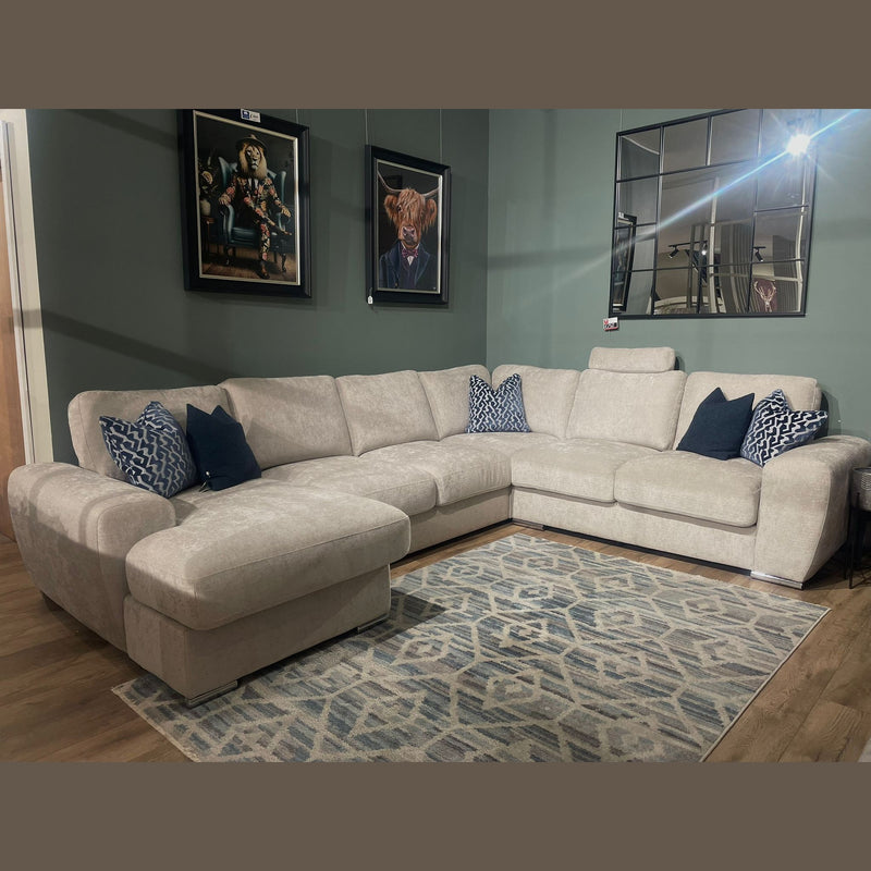 The Grand Corner Group 4L, a spacious light gray modular sectional with blue and patterned pillows, sits on a geometric rug in a modern living room with green walls, animal-themed portraits, and a grid-style mirror.