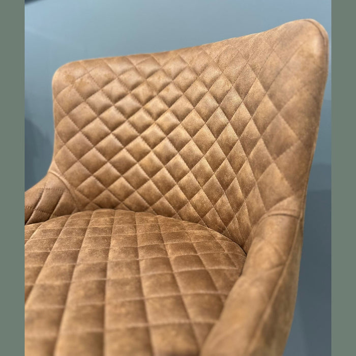 A close-up of the Diamond Dining Chair, featuring brown upholstery with a quilted pattern on the backrest and seat, set against a light blue wall.