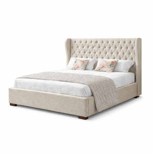 The Vienna Bedframe features a tall, tufted, winged beige headboard and is styled with white bedding, a light grey quilt, and two floral pillows. The setup is shown against a plain white background.