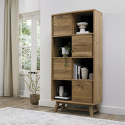 Tall, modern wooden shelving unit with open shelves and closed storage compartments, featuring a natural wood grain and angled legs.