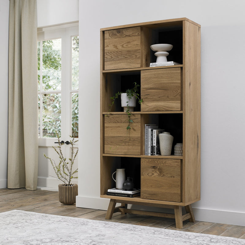 Tall, modern wooden shelving unit with open shelves and closed storage compartments, featuring a natural wood grain and angled legs.
