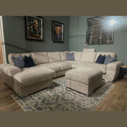 A modern living room featuring the Grand Corner Group 4L beige modular sofa, matching ottoman, patterned rug, blue and white accent pillows, dark green walls, whimsical animal wall art, and mirrored wall decor.