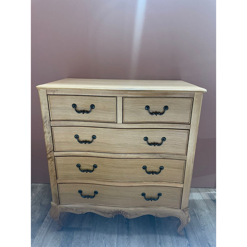 A tall chest of drawers with a beige linen upholstered headboard and carved oak wood detailing.