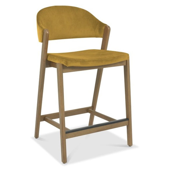 The Camden Counter Stool features a mustard yellow cushioned seat and backrest, supported by a light wood frame and footrest, displayed on a white background.