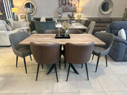 The Elson Table & 6 Diamond Chairs - Special Offer set, featuring two brown and four dark gray padded chairs, is displayed on a tiled floor in a stylish showroom with sofas, lamps, and decorative mirrors in the background.