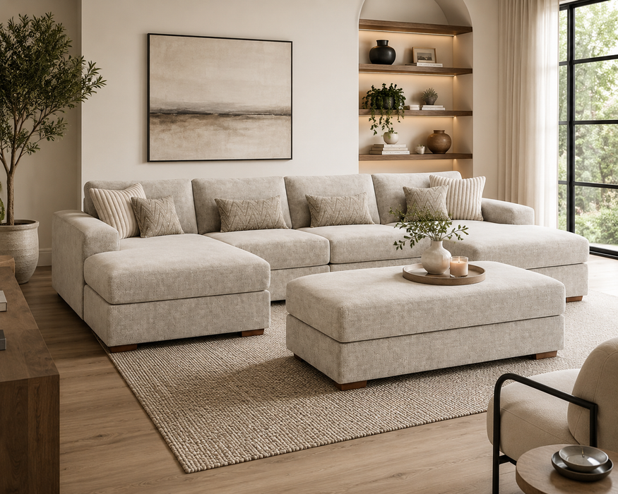 A modern living room featuring the Henley large contemporary beige chenille sofa with matching ottoman, neutral pillows, a textured rug, wall art, built-in shelves with decor, and expansive windows for natural light.