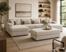 A modern living room featuring the Henley large contemporary beige chenille sofa with matching ottoman, neutral pillows, a textured rug, wall art, built-in shelves with decor, and expansive windows for natural light.