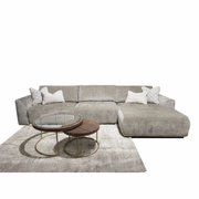 A modern living room setup featuring the Opus Chaise, a large gray modular sectional with Aquaclean Fabrics, two white patterned throw pillows, a light gray area rug, and two round nesting coffee tables with wood tops and gold metal frames.