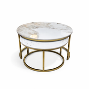 The Kas Nest - Gold Base features two round nesting coffee tables with white marble tops and gold metal frames. The modern design allows the smaller table to be partially tucked beneath the larger one, set against a plain white background.
