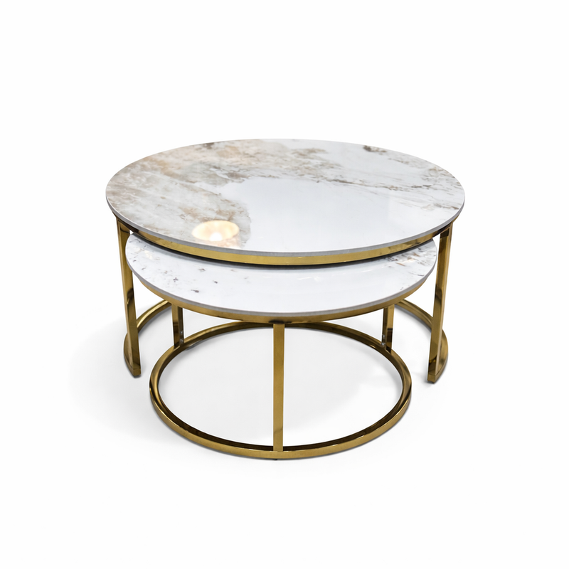 The Kas Nest - Gold Base features two round nesting coffee tables with white marble tops and gold metal frames. The modern design allows the smaller table to be partially tucked beneath the larger one, set against a plain white background.