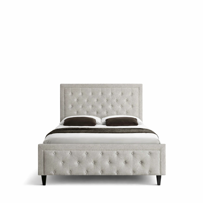 The Florence Bedframe showcases a modern design with a button-tufted light grey headboard and footboard, black legs, white bedding, and two dark throw pillows, all set against a white background for an elegant touch.