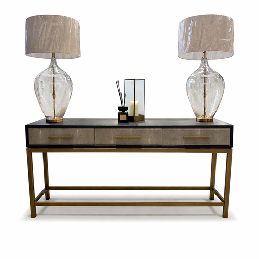 The Noir Console, a modern dark wood table with gold accents, includes three drawers and is styled with two large glass lamps with beige shades plus a centerpiece of candles and a reed diffuser.
