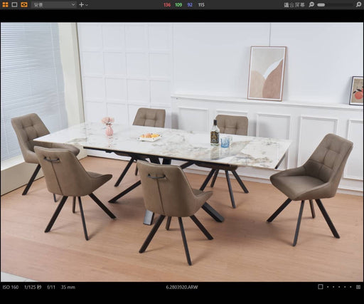 A modern dining room featuring the Sorrento Dining Table and 6 Pedro Chairs, set on light wooden flooring. Minimalist wall art and a flower vase enhance the white-paneled background.