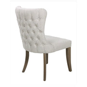 The Duke Chair features light gray upholstery, a button-tufted backrest, and dark oak legs. Shown from an angle, the image highlights the chair’s back and one side.